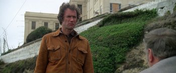 Movie still from “The Enforcer” (1976), directed by James Fargo – A person wearing a jacket near a building; Close Up shot, Low angle