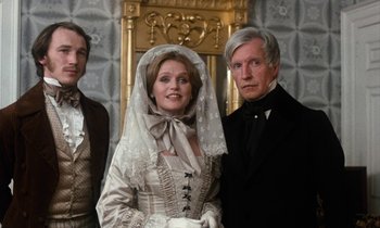 Movie still from “The Europeans” (1979), directed by James Ivory – A man and a woman standing next to each other in front of an ornate wall; Medium shot, High angle