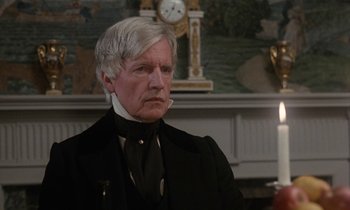 Movie still from “The Europeans” (1979), directed by James Ivory – An older man wearing a black suit and a white beard; Close Up shot, Over the shoulder angle
