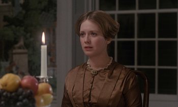 Movie still from “The Europeans” (1979), directed by James Ivory – A woman in a brown dress sitting in front of a candle; Close Up shot, Over the shoulder angle