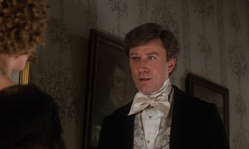 Movie still from “The Europeans” (1979), directed by James Ivory – A man wearing a suit and a bow tie in front of a painting; Close Up shot, Over the shoulder angle