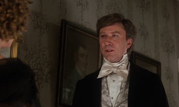 Movie still from “The Europeans” (1979), directed by James Ivory – A man wearing a suit and bow tie in front of a portrait; Close Up shot, Over the shoulder angle