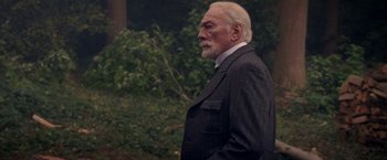 Movie still from “The Exception” (2016), directed by David Leveaux – An older man in a suit is looking off into the distance; Medium shot, Over the shoulder angle
