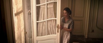 Movie still from “The Exception” (2016), directed by David Leveaux – A woman standing in front of an open door; Medium shot, Low angle