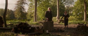 Movie still from “The Exception” (2016), directed by David Leveaux – An old man in a suit is standing in the woods; Wide shot, Over the shoulder angle