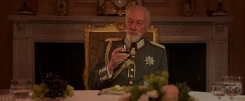 Movie still from “The Exception” (2016), directed by David Leveaux – An older man in a military uniform holding a glass of red wine; Medium shot, Low angle