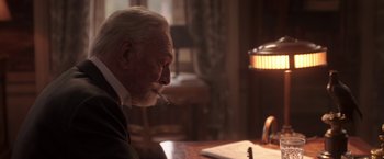 Movie still from “The Exception” (2016), directed by David Leveaux – An older man sitting at a table smoking a cigarette; Close Up shot, Over the shoulder angle