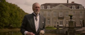 Movie still from “The Exception” (2016), directed by David Leveaux – An older man wearing a suit and tie holding a towel; Medium shot, Low angle