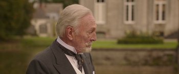 Movie still from “The Exception” (2016), directed by David Leveaux – An old man with a beard wearing a suit and tie; Close Up shot, Over the shoulder angle