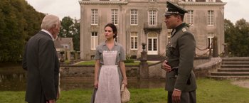 Movie still from “The Exception” (2016), directed by David Leveaux – A man and a woman standing in front of a building; Medium shot, Over the shoulder angle