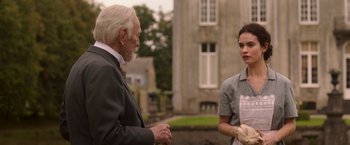 Movie still from “The Exception” (2016), directed by David Leveaux – An older man and a young woman standing next to each other; Medium shot, Over the shoulder angle