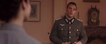 Movie still from “The Exception” (2016), directed by David Leveaux – A man in a military uniform standing in front of a wall; Medium shot, Over the shoulder angle
