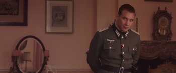 Movie still from “The Exception” (2016), directed by David Leveaux – A man in a military uniform standing next to a wall; Medium shot, Over the shoulder angle