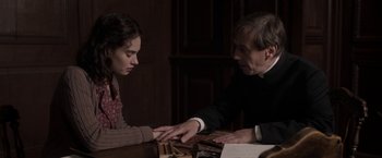 Movie still from “The Exception” (2016), directed by David Leveaux – An older man and a young woman are touching hands; Medium shot, Over the shoulder angle