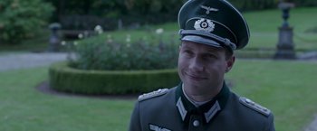 Movie still from “The Exception” (2016), directed by David Leveaux – A man in a uniform is smiling for the camera; Close Up shot, Over the shoulder angle