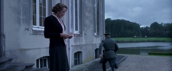 Movie still from “The Exception” (2016), directed by David Leveaux – An older woman standing next to an older man; Medium shot, Low angle