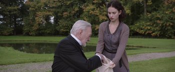 Movie still from “The Exception” (2016), directed by David Leveaux – An older man and a young woman holding a bag; Medium shot, Over the shoulder angle