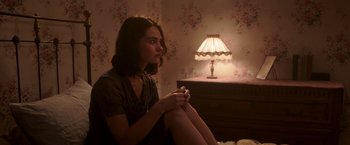 Movie still from “The Exception” (2016), directed by David Leveaux – A woman sitting on a bed in front of a lamp; Medium shot, High angle