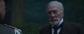 Movie still from “The Exception” (2016), directed by David Leveaux – An old man with a beard and a suit and tie; Close Up shot, Over the shoulder angle