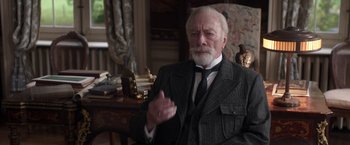 Movie still from “The Exception” (2016), directed by David Leveaux – An older man wearing a suit and a tie; Medium shot, High angle