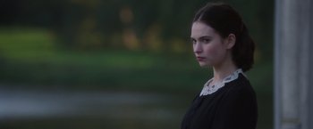 Movie still from “The Exception” (2016), directed by David Leveaux – A woman in a black dress is standing in front of a body of water; Close Up shot, Over the shoulder angle