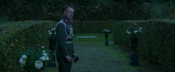Movie still from “The Exception” (2016), directed by David Leveaux – A man in a uniform standing in the grass; Medium shot, Over the shoulder angle