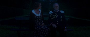Movie still from “The Exception” (2016), directed by David Leveaux – A man and a woman sitting next to each other on a bench; Medium shot, Low angle