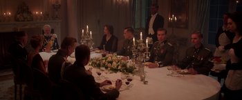 Movie still from “The Exception” (2016), directed by David Leveaux – A group of people sitting at a table with candles on it; Wide shot, High angle