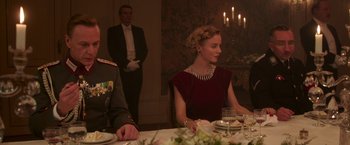 Movie still from “The Exception” (2016), directed by David Leveaux – A woman sitting at a table in front of a man; Medium shot, Low angle