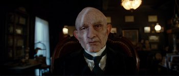 Movie still from “The Extraordinary Adventures of Adèle Blanc-Sec” (2010), directed by Luc Besson – An old man with a bald head wearing a suit and tie; Close Up shot, Low angle