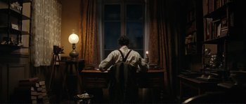 Movie still from “The Extraordinary Adventures of Adèle Blanc-Sec” (2010), directed by Luc Besson – A man sitting at a desk in front of a window; Wide shot, High angle