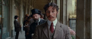 Movie still from “The Extraordinary Adventures of Adèle Blanc-Sec” (2010), directed by Luc Besson – A man in a suit and a tie standing next to another man in a hat; Close Up shot, Low angle
