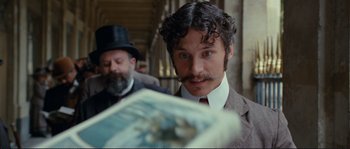 Movie still from “The Extraordinary Adventures of Adèle Blanc-Sec” (2010), directed by Luc Besson – A man in a suit and a top hat looking at a newspaper; Close Up shot, Low angle