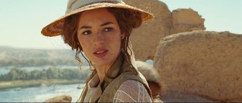 Movie still from “The Extraordinary Adventures of Adèle Blanc-Sec” (2010), directed by Luc Besson – A young woman wearing a hat standing in front of a rock wall; Close Up shot, Over the shoulder angle