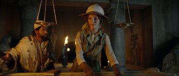 Movie still from “The Extraordinary Adventures of Adèle Blanc-Sec” (2010), directed by Luc Besson – A woman sitting on top of a table in front of a lamp; Medium shot, Low angle