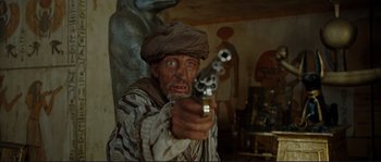Movie still from “The Extraordinary Adventures of Adèle Blanc-Sec” (2010), directed by Luc Besson – A man holding a gun in a room with statues; Medium shot, Over the shoulder angle
