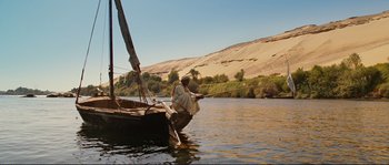 Movie still from “The Extraordinary Adventures of Adèle Blanc-Sec” (2010), directed by Luc Besson – A man sitting on the side of a boat in the middle of a river; Extreme Wide shot, Low angle