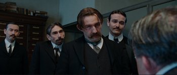 Movie still from “The Extraordinary Adventures of Adèle Blanc-Sec” (2010), directed by Luc Besson – A group of men in suits and ties standing next to each other; Medium shot, Low angle