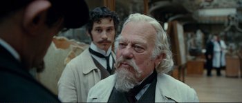 Movie still from “The Extraordinary Adventures of Adèle Blanc-Sec” (2010), directed by Luc Besson – A man with long white hair and a beard standing next to another man with long white hair; Close Up shot, Over the shoulder angle