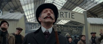Movie still from “The Extraordinary Adventures of Adèle Blanc-Sec” (2010), directed by Luc Besson – A man in a suit and hat holding a cane; Close Up shot, Low angle