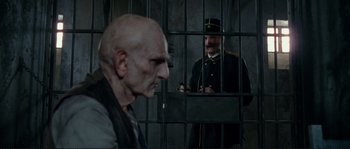 Movie still from “The Extraordinary Adventures of Adèle Blanc-Sec” (2010), directed by Luc Besson – A man in a prison uniform standing in front of another man in a jail cell behind bars; Close Up shot, Over the shoulder angle