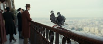 Movie still from “The Extraordinary Adventures of Adèle Blanc-Sec” (2010), directed by Luc Besson – Two pigeons sitting on a railing in front of a city skyline; Close Up shot, Low angle
