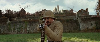 Movie still from “The Extraordinary Adventures of Adèle Blanc-Sec” (2010), directed by Luc Besson – A man in a hat holding a rifle in his hands; Medium shot, Low angle