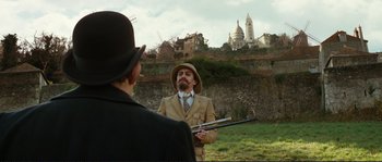 Movie still from “The Extraordinary Adventures of Adèle Blanc-Sec” (2010), directed by Luc Besson – A man with a beard and a hat is holding a rifle; Wide shot, Over the shoulder angle