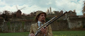 Movie still from “The Extraordinary Adventures of Adèle Blanc-Sec” (2010), directed by Luc Besson – A man in a suit and hat holding a rifle; Medium shot, Low angle