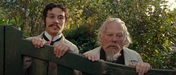 Movie still from “The Extraordinary Adventures of Adèle Blanc-Sec” (2010), directed by Luc Besson – Two men standing next to each other in front of a forest; Medium shot, Low angle