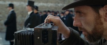 Movie still from “The Extraordinary Adventures of Adèle Blanc-Sec” (2010), directed by Luc Besson – A man in a hat is holding an old camera; Close Up shot, Low angle