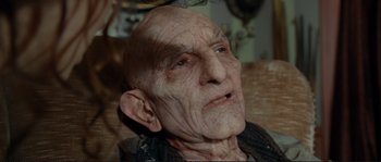 Movie still from “The Extraordinary Adventures of Adèle Blanc-Sec” (2010), directed by Luc Besson – An old man is sitting on a table; Close Up shot, High angle