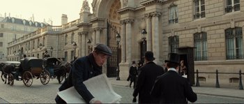 Movie still from “The Extraordinary Adventures of Adèle Blanc-Sec” (2010), directed by Luc Besson – An old man is reading a newspaper in front of a large building; Wide shot, Over the shoulder angle