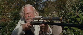 Movie still from “The Extraordinary Adventures of Adèle Blanc-Sec” (2010), directed by Luc Besson – An old man with a long white beard holding a rifle; Close Up shot, Low angle